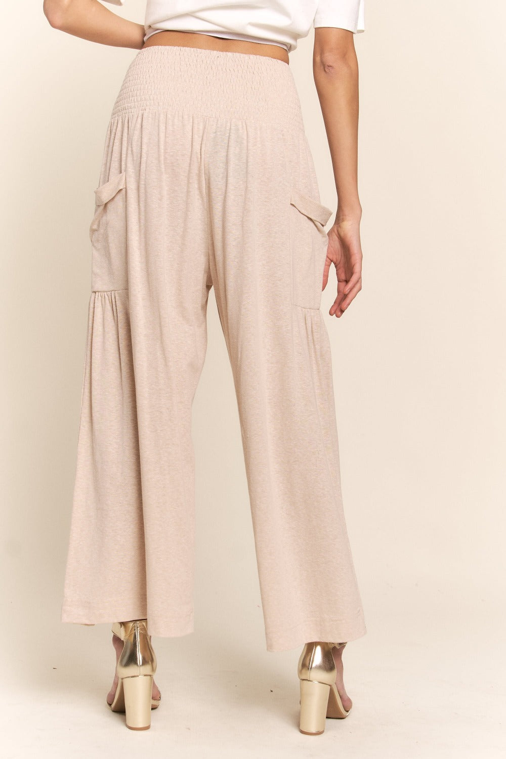 Woman wearing J.NNA smocked waist boho wide leg pants with pockets, showcasing comfortable and stylish design.