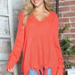 Woman wearing Bella Road frayed hem dropped shoulder sweater in vibrant orange. Perfect blend of quirky fun and comfort.