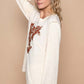 Woman modeling a cream embroidered long sleeve knit top with intricate floral detailing against a neutral background.