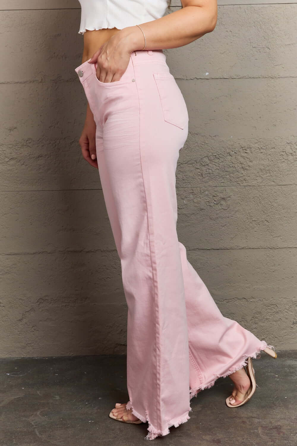 Woman modeling Raelene High Waist Wide Leg Jeans in light pink with frayed hem by Risen Jeans, showcasing a flattering high-rise fit.