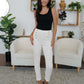 Woman wearing FAM-FAM high waist skinny pants in white, featuring decorative buttons, styled with a black top in a chic living room.