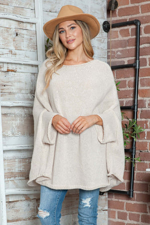 Woman wearing Bella Road round neck batwing sleeve sweater with a stylish hat, standing by a rustic wall.