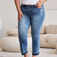 Woman wearing Judy Blue release hem cropped bootcut jeans standing in a stylish living room with white furniture.