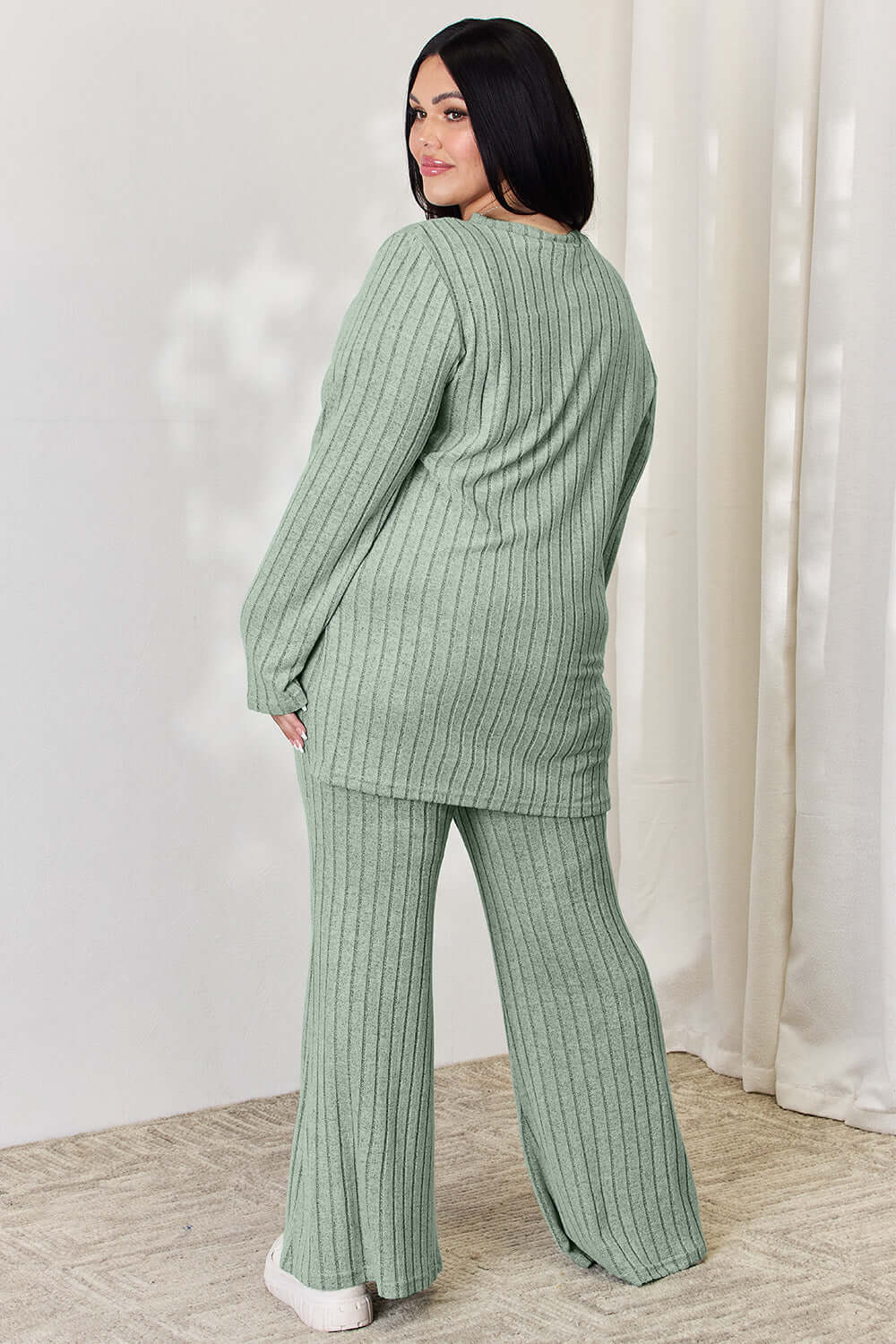 Back view of woman wearing a ribbed high-low top and wide leg pants set in green, made of slightly stretchy polyester and elastane.