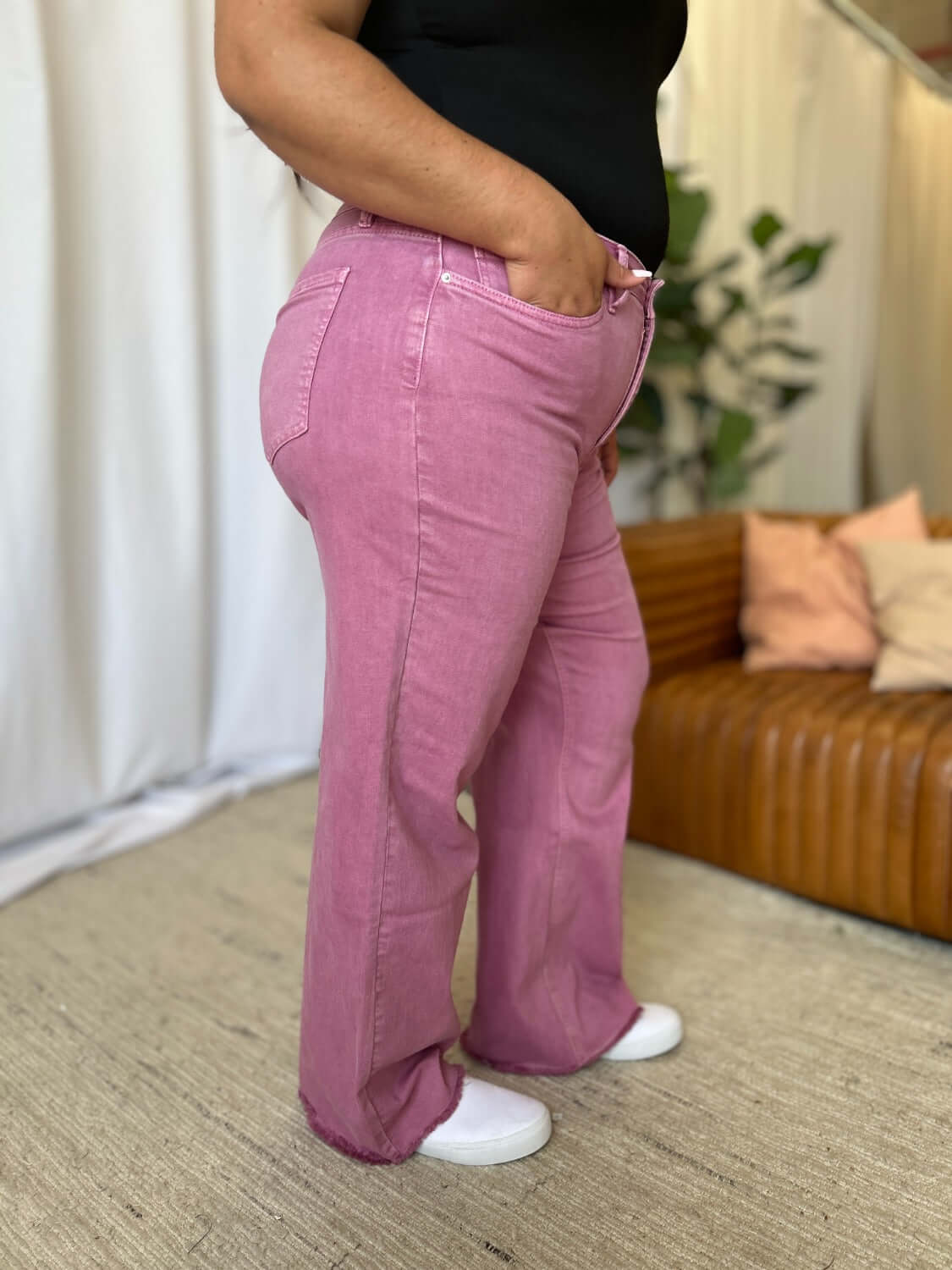 Woman wearing RFM Full Size High Rise Garment Dye Wide Leg Jeans in pink, showcasing relaxed fit and unique color indoors.