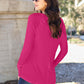 Woman wearing round neck long sleeve T-shirt in pink, viewed from the back, standing outdoors.