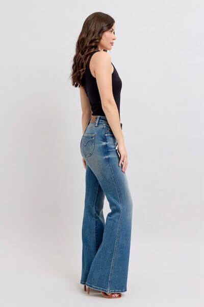 Side view of a model in Judy Blue mid rise tummy control vintage wash jeans paired with a black tank top.