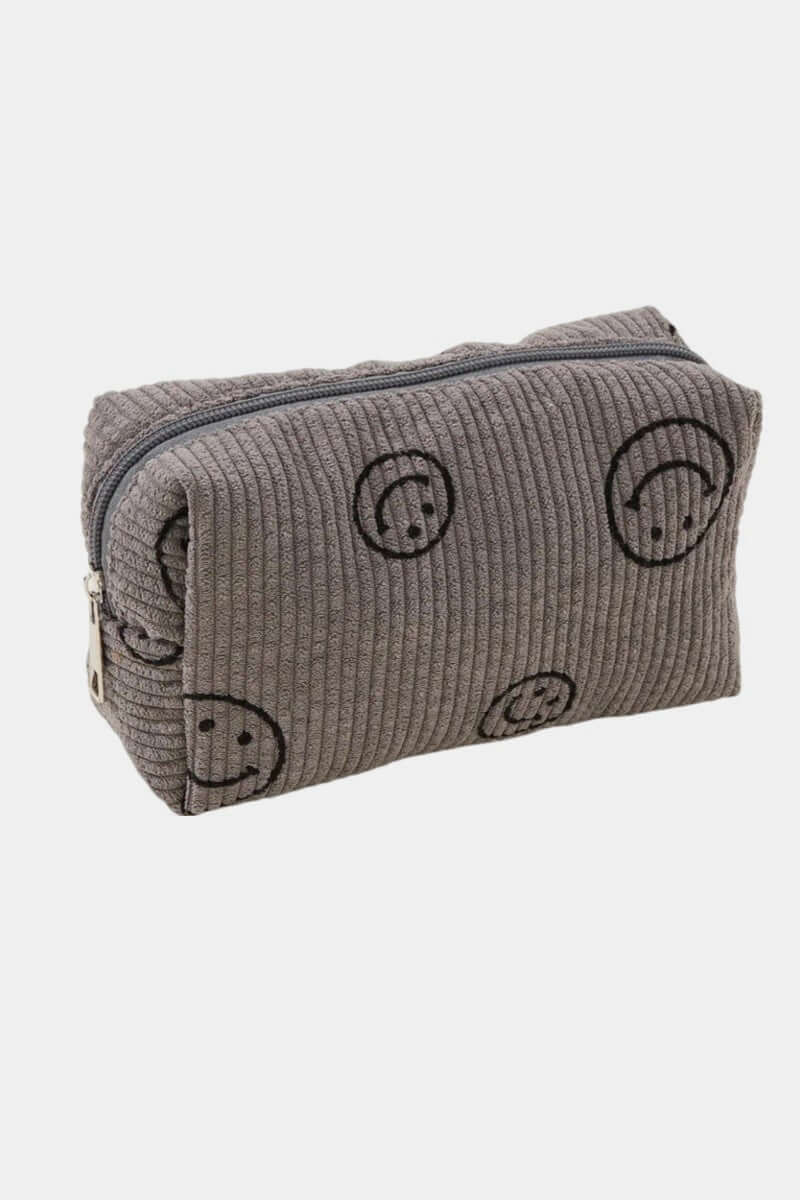 Small corduroy cosmetic pouch with embroidered smiley faces, perfect for storing makeup essentials on the go.