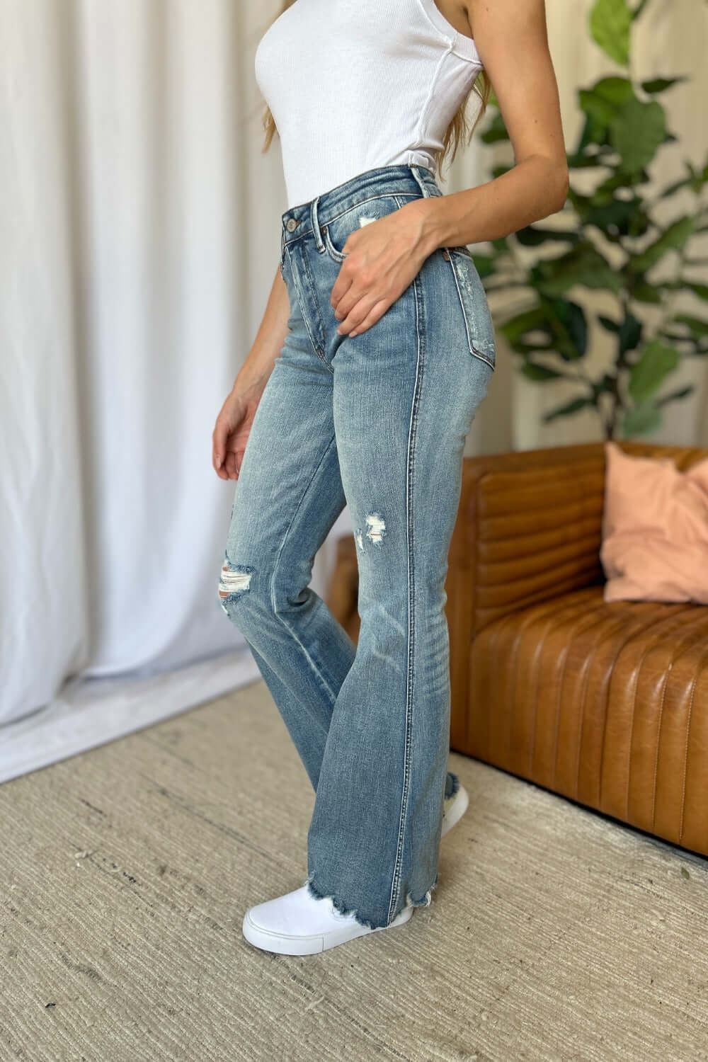 Woman wearing Judy Blue medium rise tummy control destroy flare jeans in a stylish home setting.