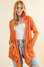 Woman wearing And The Why full size thermal hooded open front cardigan with pockets in orange over white top and jeans.