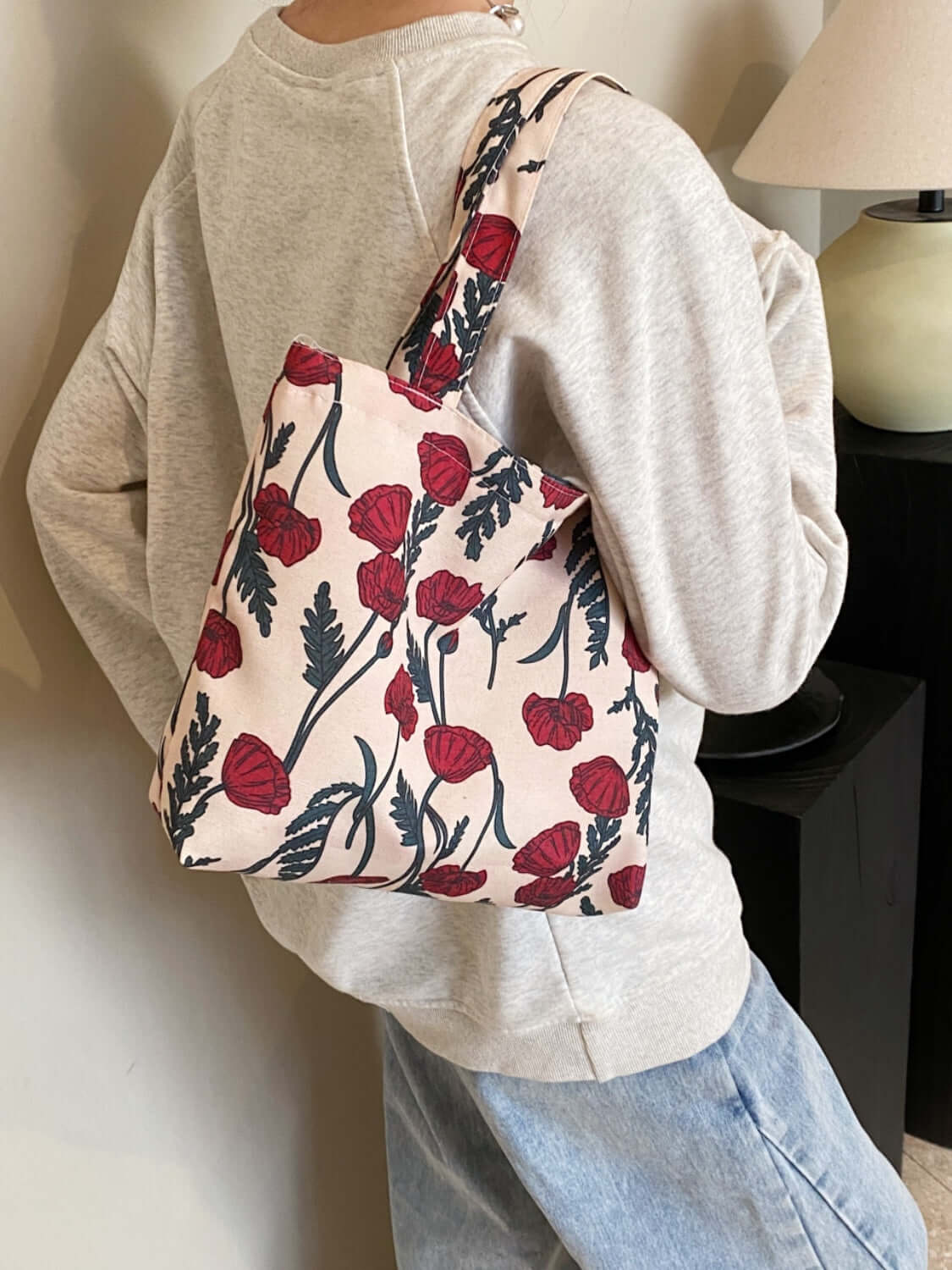 Person wearing a medium-sized printed canvas handbag with zipper, featuring red floral design. Perfect for a casual day out.