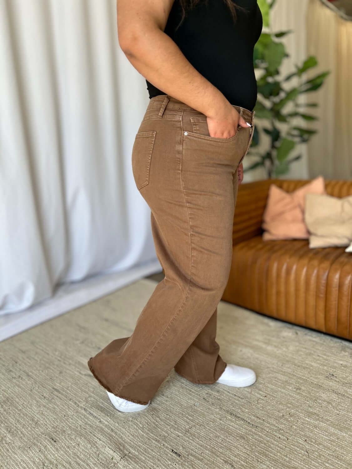 Woman wearing RFM full size high rise garment dye wide leg jeans with relaxed silhouette and rich color, standing in stylish indoor setting.