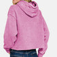 Woman wearing a pink Zenana Acid Wash Fleece Cropped Hoodie, showcasing a trendy and vintage-inspired style.