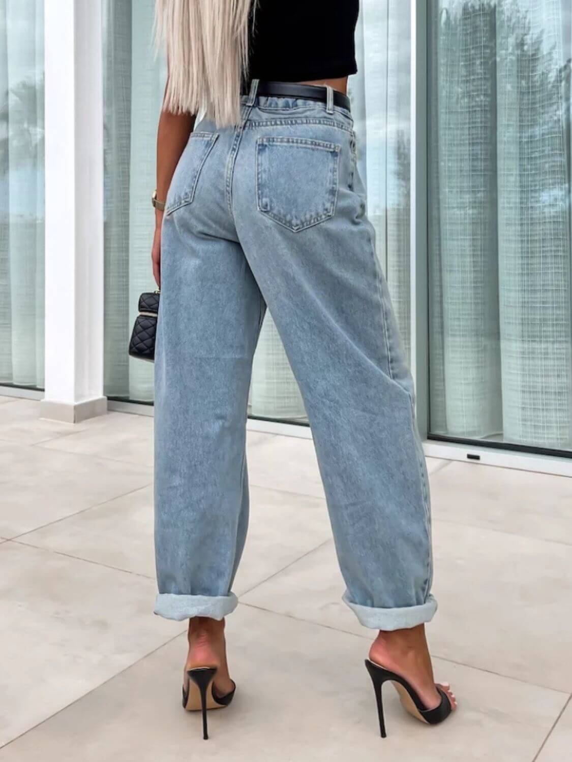 Woman wearing high waist wide leg jeans with rolled cuffs and black heels, showing back view.