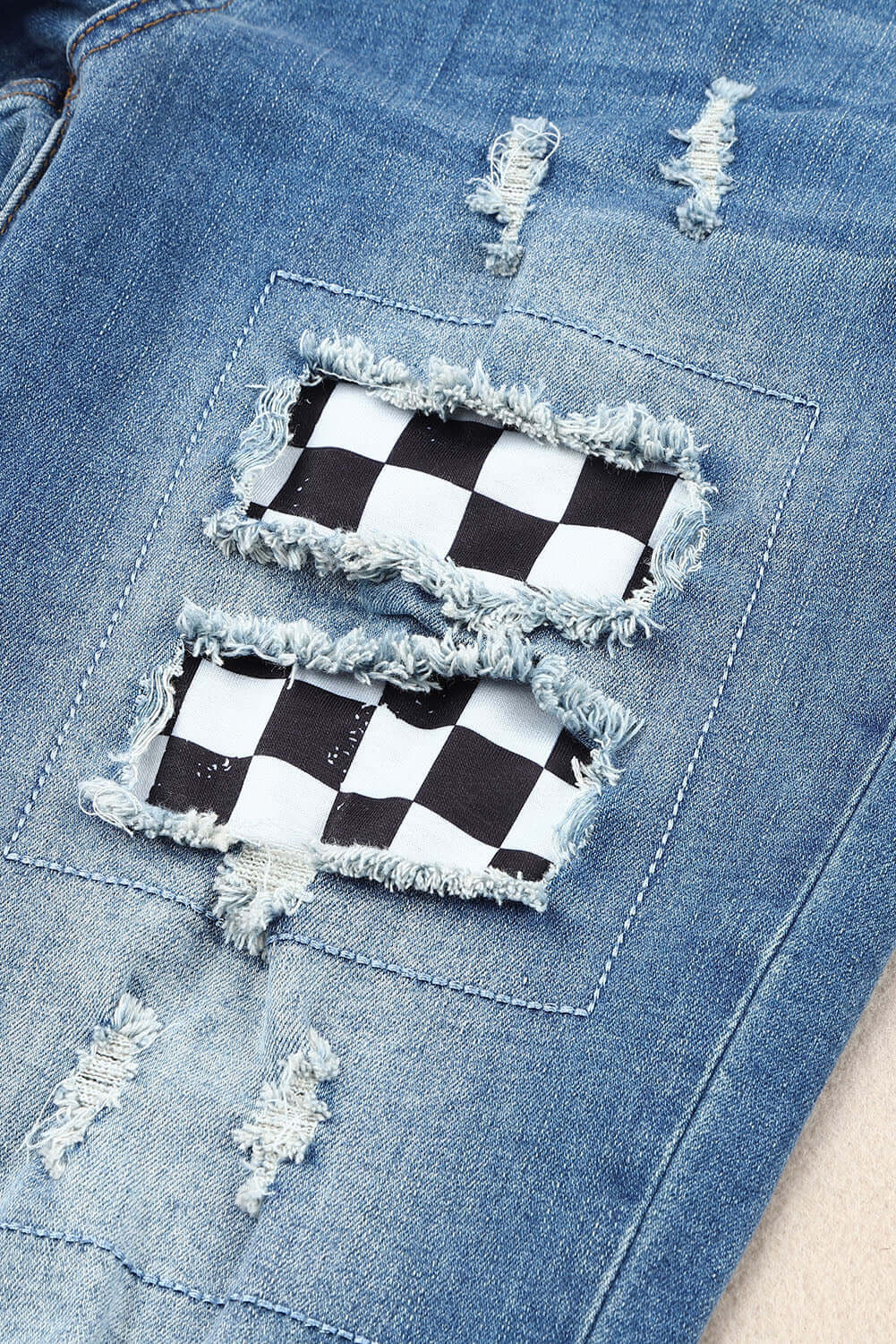 Checkered patchwork on distressed denim jeans with frayed details. Trendy mid-waist jeans for a stylish and edgy look.