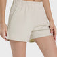 Millennia Elastic Waist Active Shorts in light beige, showcasing a comfortable fit and handy side pockets. Perfect for active wear!