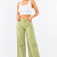 Model wearing high waist distressed wide leg jeans in olive green, paired with a white crop top for a trendy look.