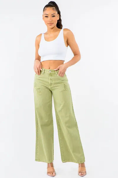 Model wearing high waist distressed wide leg jeans in olive green, paired with a white crop top for a trendy look.