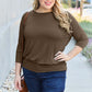 Woman wearing a brown round neck batwing sleeve top and blue jeans outdoors