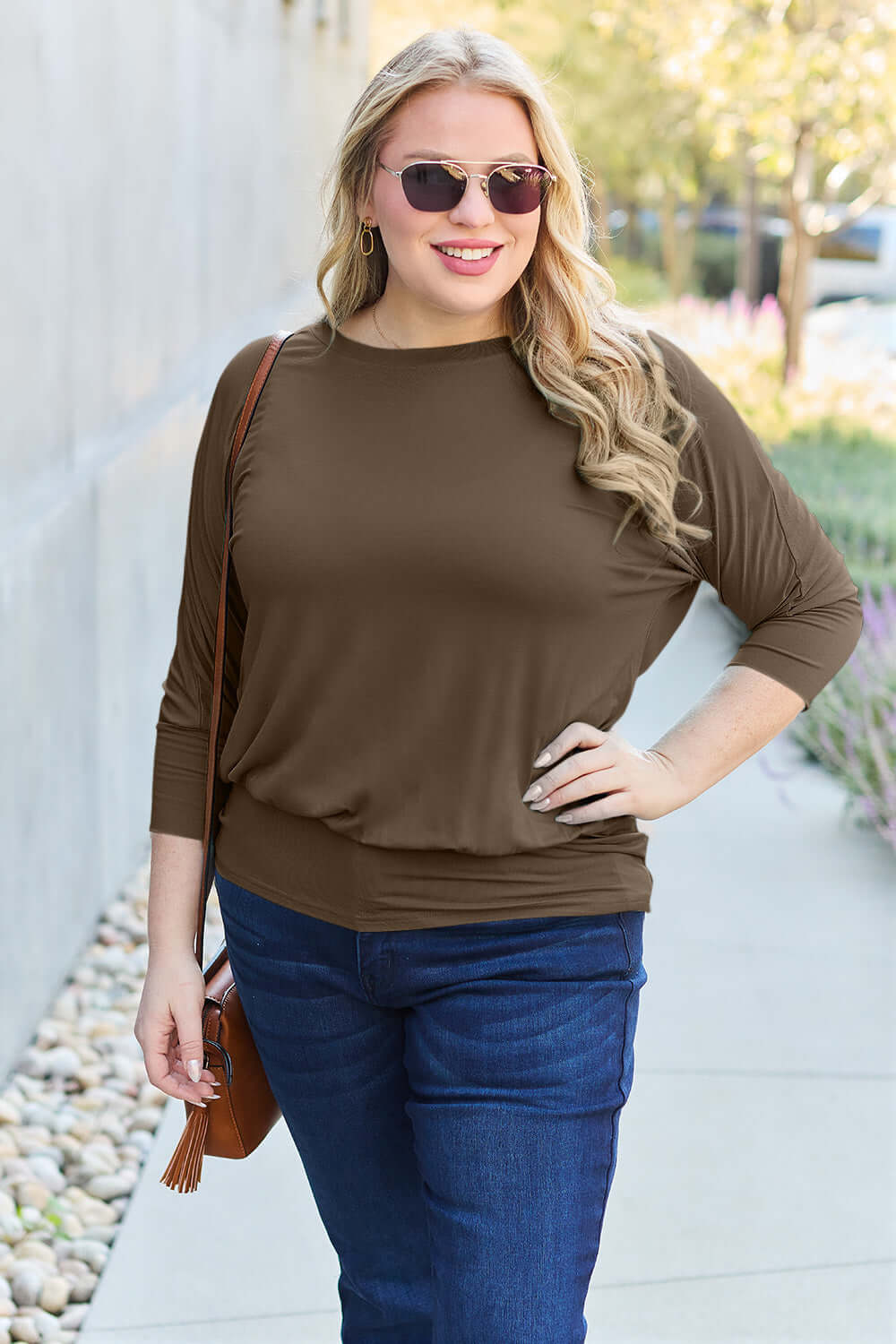 Woman wearing a brown round neck batwing sleeve top and blue jeans outdoors