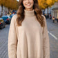 Woman wearing a cozy turtleneck sweater with side slits and dropped shoulders, perfect for fall fashion on a sunny day in the city.