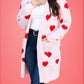 Woman wearing Bella Road Heart Open Front Long Sleeve Cardigan with red hearts over white top and jeans on pink background