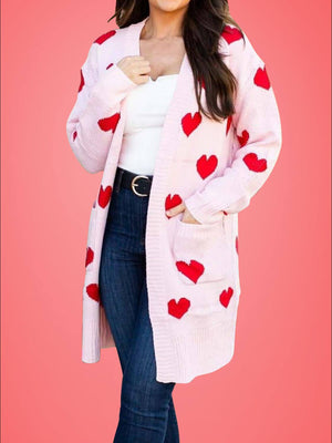 Woman wearing Bella Road Heart Open Front Long Sleeve Cardigan with red hearts over white top and jeans on pink background