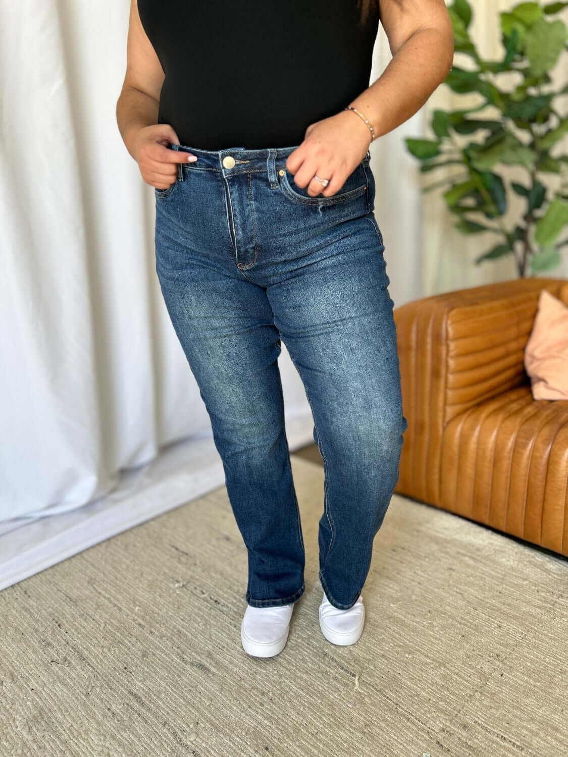 Woman wearing RFM Full Size High Rise Straight Tummy Control Jeans in a living room setting, displaying the jeans' flattering high-waist and straight-leg cut.