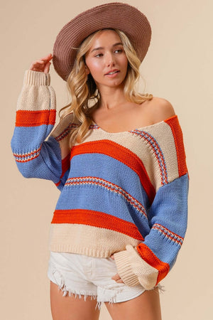 Woman wearing BiBi Multi Color Stripe Scoop Neck Sweater with vibrant red, blue, and beige stripes, paired with a hat and white shorts.