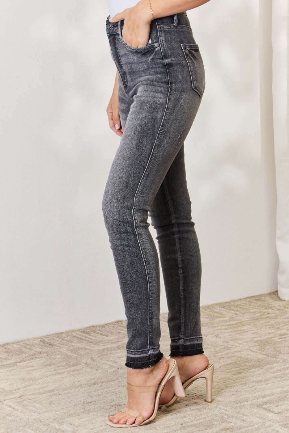 Woman wearing high waist tummy control release hem skinny Judy Blue Jeans, showcasing side view with black color and premium stretch fabric.