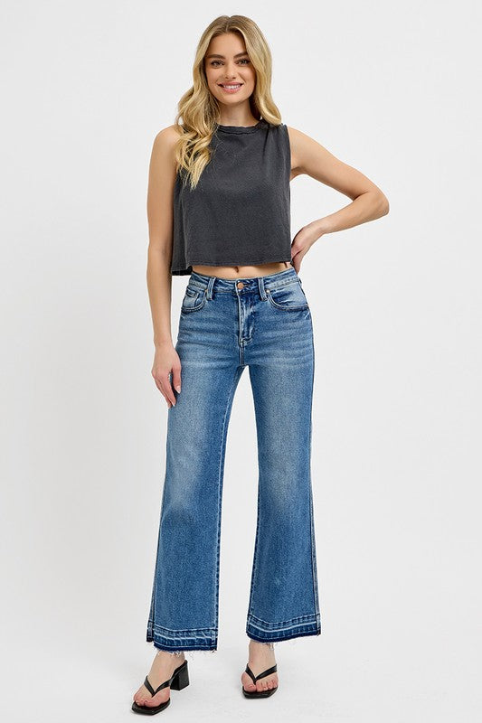 Trendy woman wearing RISEN raw hem ankle bootcut jeans with a stylish crop top and heels, showcasing a chic, casual look.