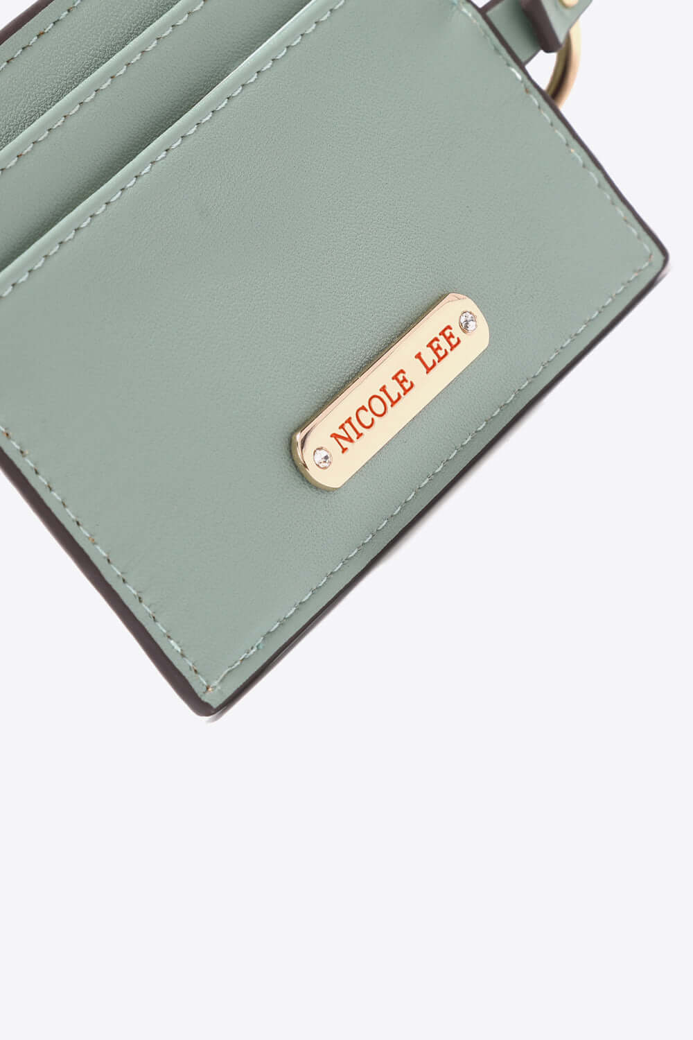 Close-up of a green Nicole Lee USA vegan leather accessory with gold logo plaque.