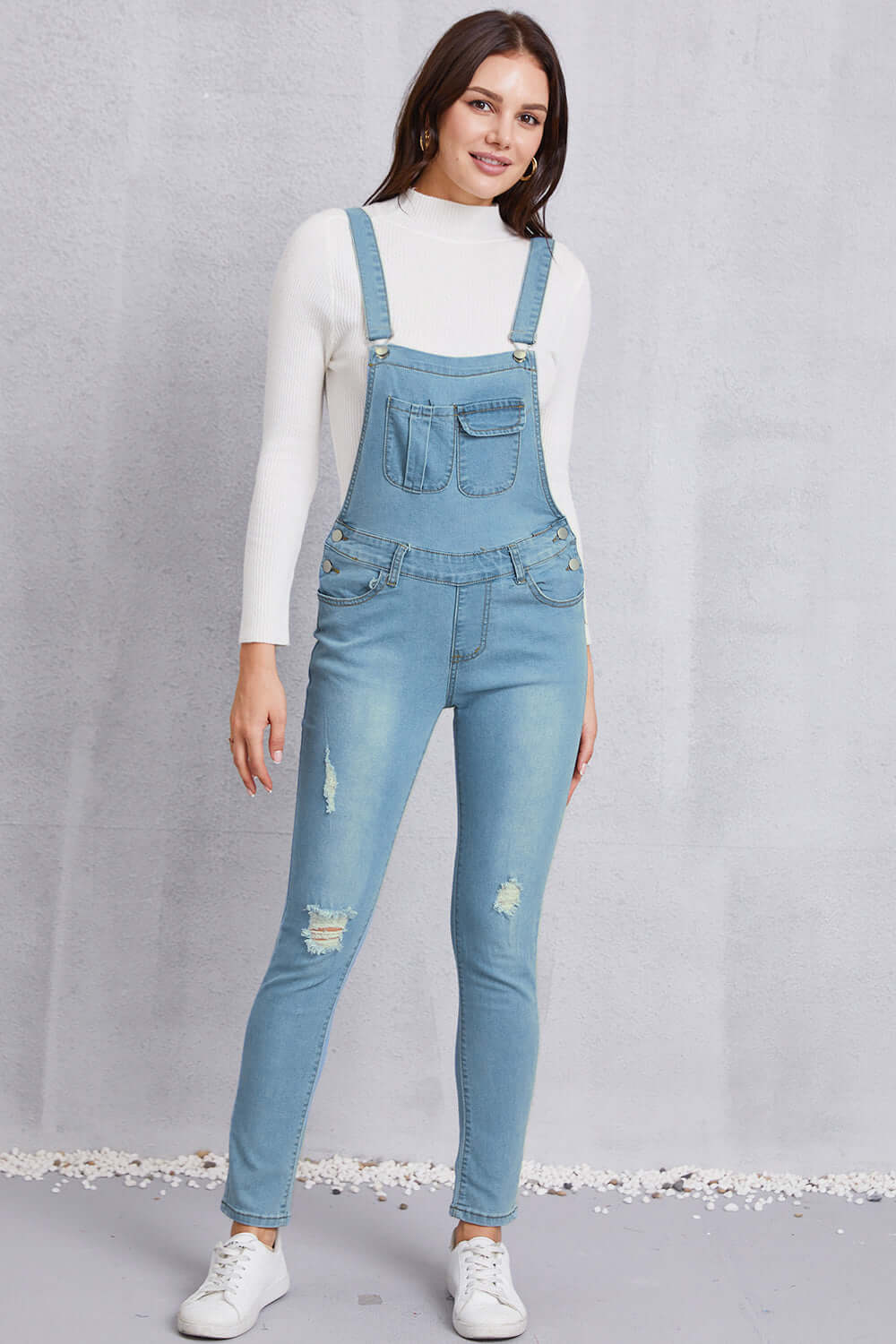 Woman wearing distressed washed denim overalls with pockets, mid waist, slightly stretchy, made of 65% cotton and 35% polyester.