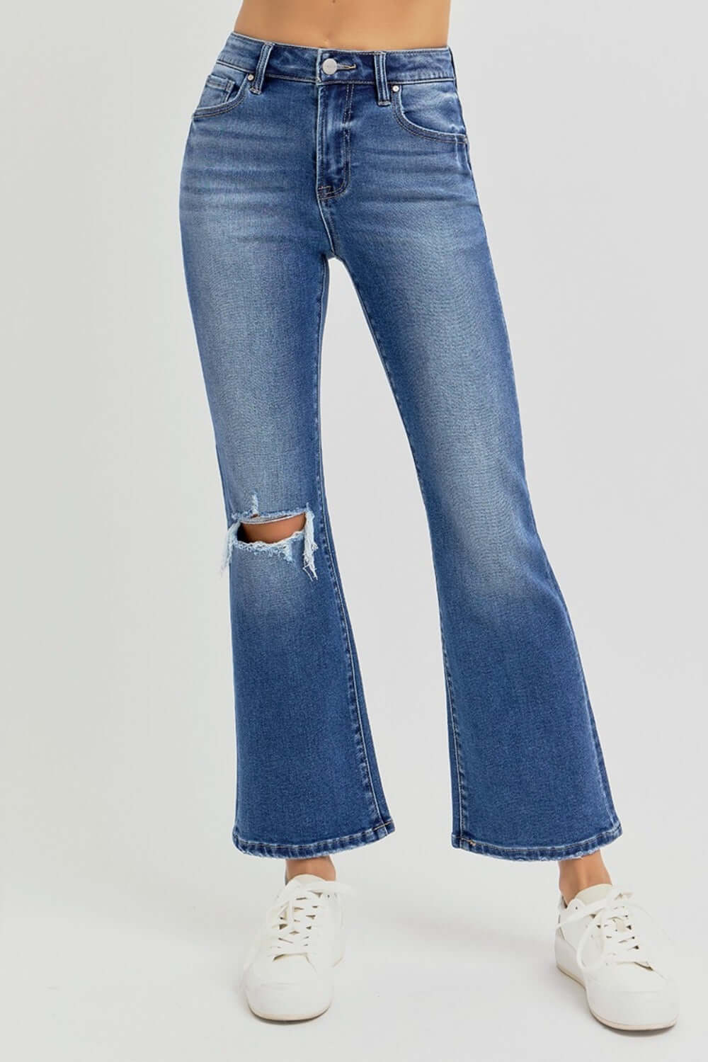 Distressed high-rise crop flare jeans with a trendy ripped knee, worn with white sneakers for a chic, effortless look.