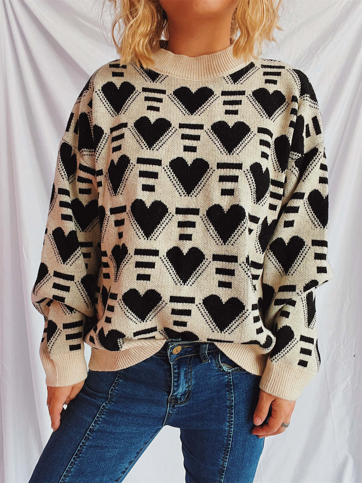 Woman wearing Bella Road Heart Contrast Long Sleeve Dropped Shoulder Sweater with heart pattern and blue jeans