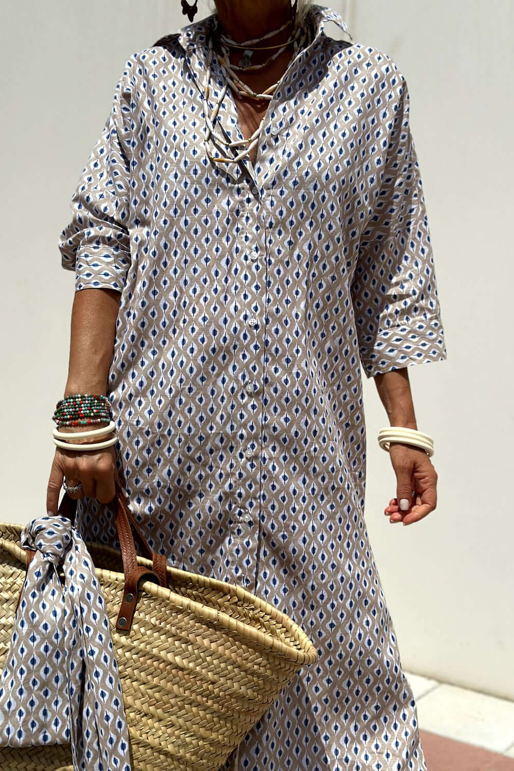 Woman wearing Bella Road Tied Button Up Three-Quarter Sleeve Dress holding a woven bag and accessorized with bracelets