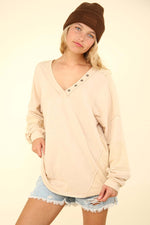 Beige VERY J Washed V-Neck Exposed Seam Knit Top with Button Trim, Drop Shoulders, and Long Sleeves Worn by Woman in Denim Shorts and Beanie