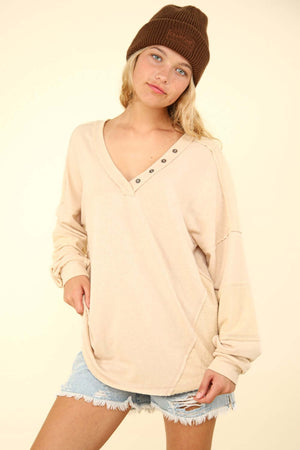 Beige VERY J Washed V-Neck Exposed Seam Knit Top with Button Trim, Drop Shoulders, and Long Sleeves Worn by Woman in Denim Shorts and Beanie