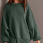 Woman wearing green Double Take Side Slit Round Neck Long Sleeve Sweater with moderate stretch and playful side slit design.