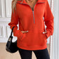 Woman wearing Ivy Lane Half Zip Raglan Sleeve Sweatshirt in vibrant orange with front pockets and black shorts.