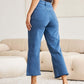 Woman wearing Crop Chloe Full Size Tummy Control High Waist Raw Hem RFM Jeans, showing back view in modern living room setting