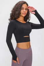 Woman in a black long-sleeved cropped top with cutout detail, showcasing stylish athletic wear perfect for workouts.