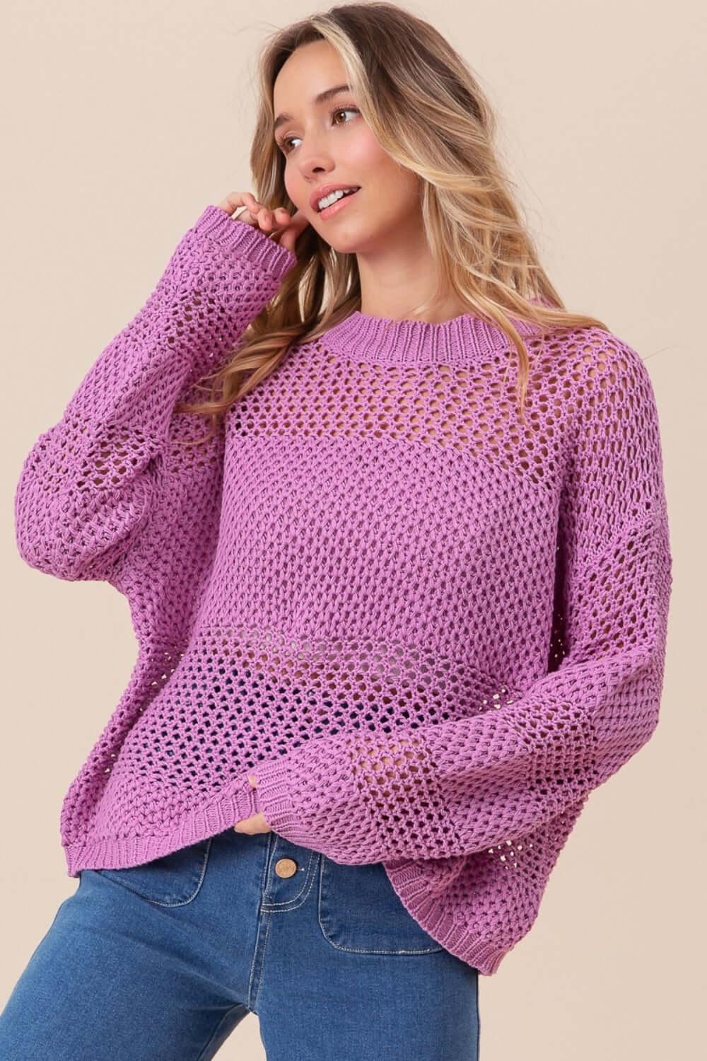 Woman wearing BiBi Openwork Long Sleeve Knit Top in purple, showcasing intricate openwork details and long sleeves, styled with blue jeans.