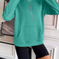 Ivy Lane Half Zip Raglan Sleeve Sweatshirt in green with front pocket, displayed indoors on model wearing black shorts.