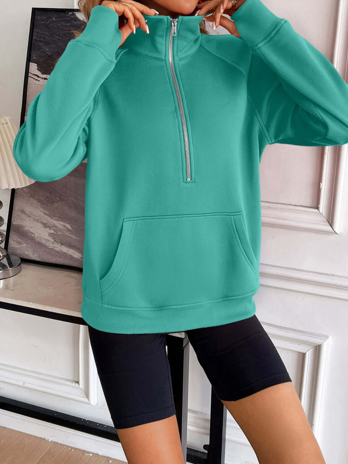 Ivy Lane Half Zip Raglan Sleeve Sweatshirt in green with front pocket, displayed indoors on model wearing black shorts.