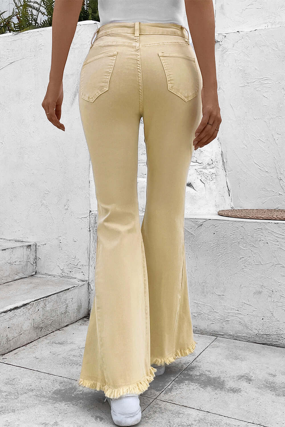 Woman wearing Bella Road Pocketed Raw Hem Flare Jeans in yellow, back view showing slightly stretchy, raw hem flare with pockets