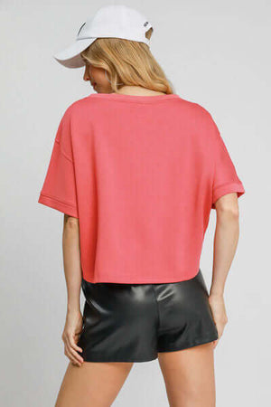 Back view of a lightweight cropped sweatshirt in coral paired with black shorts, showcasing casual style.