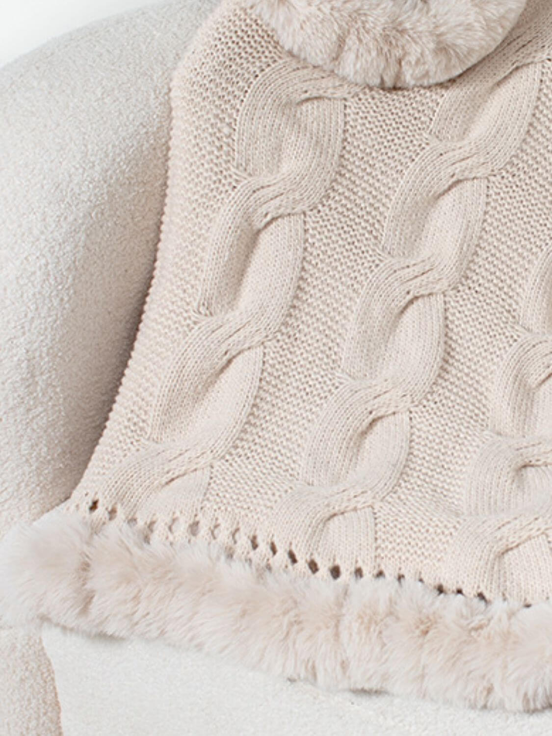 Soft beige Bella Road fuzzy hem cable-knit poncho draped on a chair, showcasing its cozy texture and stylish design.