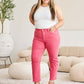 Woman wearing pink high-waist raw hem RFM jeans and white tank top, standing in a stylish, modern living room.