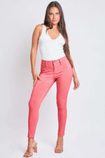 Woman wearing YMI Jeans Hyperstretch Mid-Rise Skinny Jeans in coral, paired with a white tank top and heels, showcasing a trendy look.